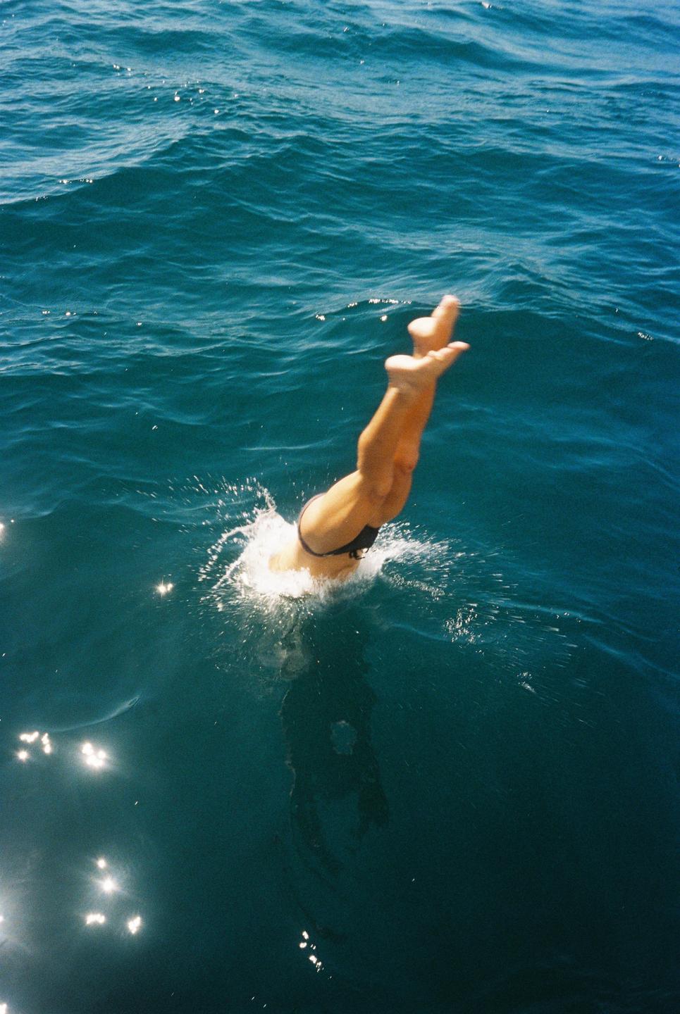 A person dives into the ocean, with their legs and feet visible above the water as they create a splash.