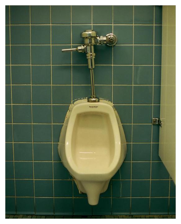 A urinal is mounted on a tiled wall.