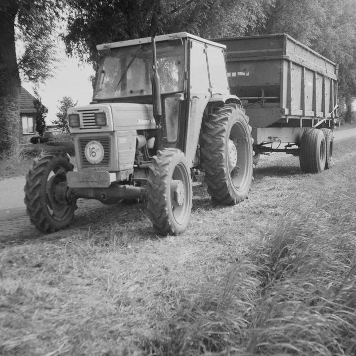 A tractor with a trailer is parked on a grassy path next to a road.