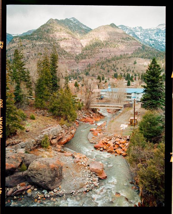 A river flows through a valley with mountains and a small town in the background.