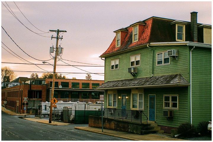 A green house with a red roof stands next to a street with a utility pole and power lines.