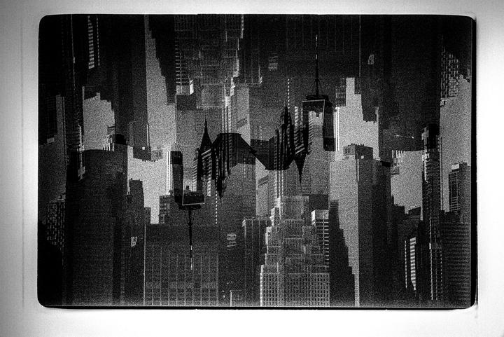 A black and white image shows a cityscape with many tall buildings and a dark, textured sky.