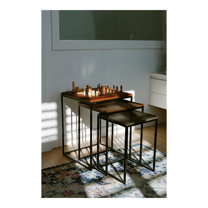 A chess set sits on a nesting table in a sunlit room with a patterned rug.