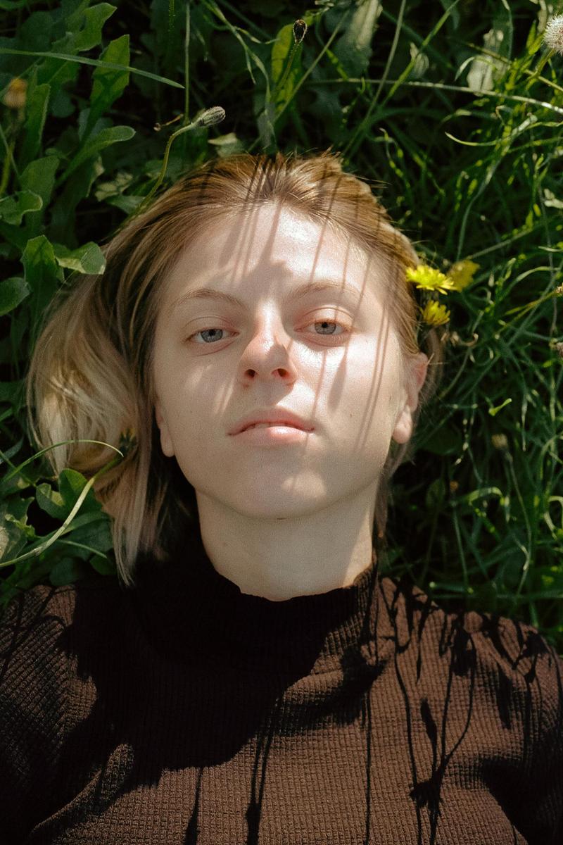 A woman with blonde hair lies in green grass with shadows cast across her face.