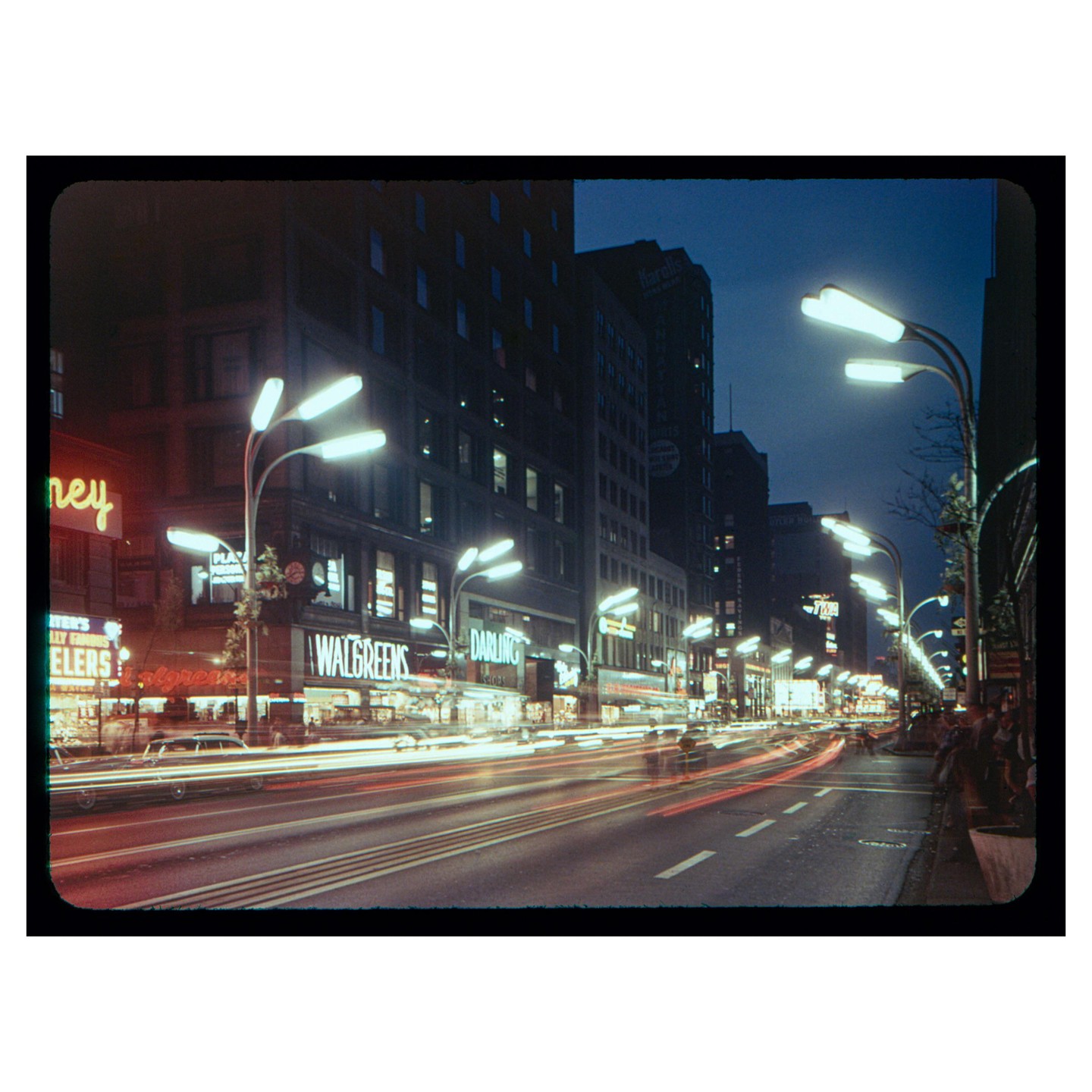 A long exposure shot of State Street in Chicago at night shows light trails from vehicles and illuminated storefronts.