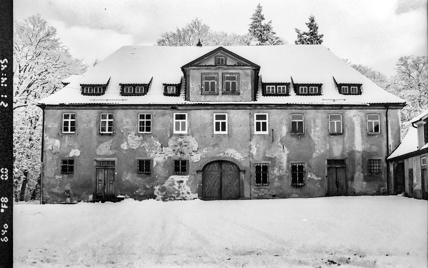 A large, snow-covered building with many windows and a central arched doorway stands in a snowy landscape.
