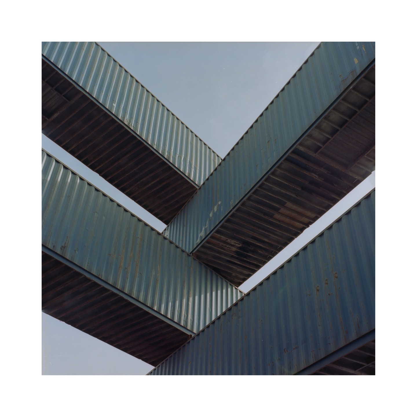 A low angle view shows several blue shipping containers stacked and angled against a clear sky.