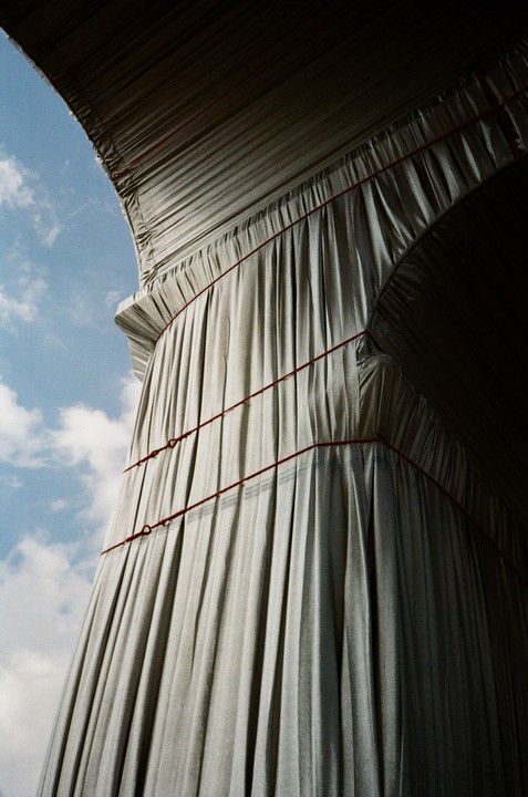 A large structure draped in fabric with red ropes is viewed from below against a blue sky with clouds.