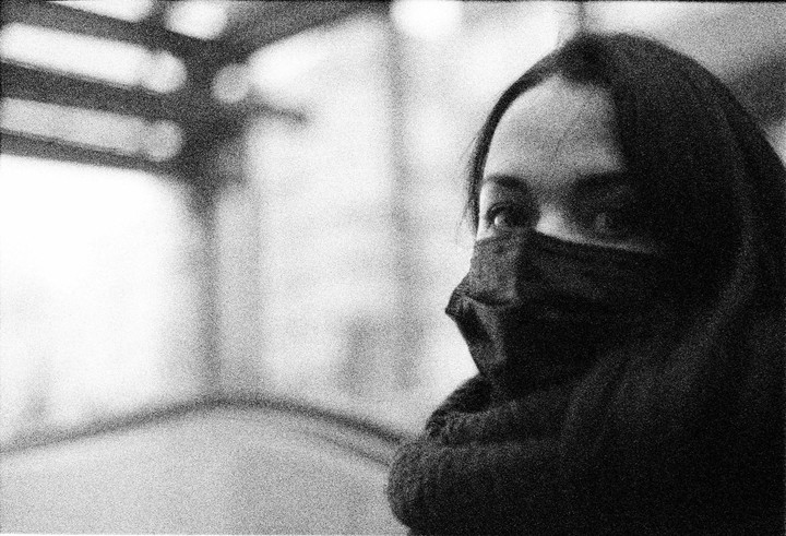 A woman wearing a face mask looks to the right with a blurred background.