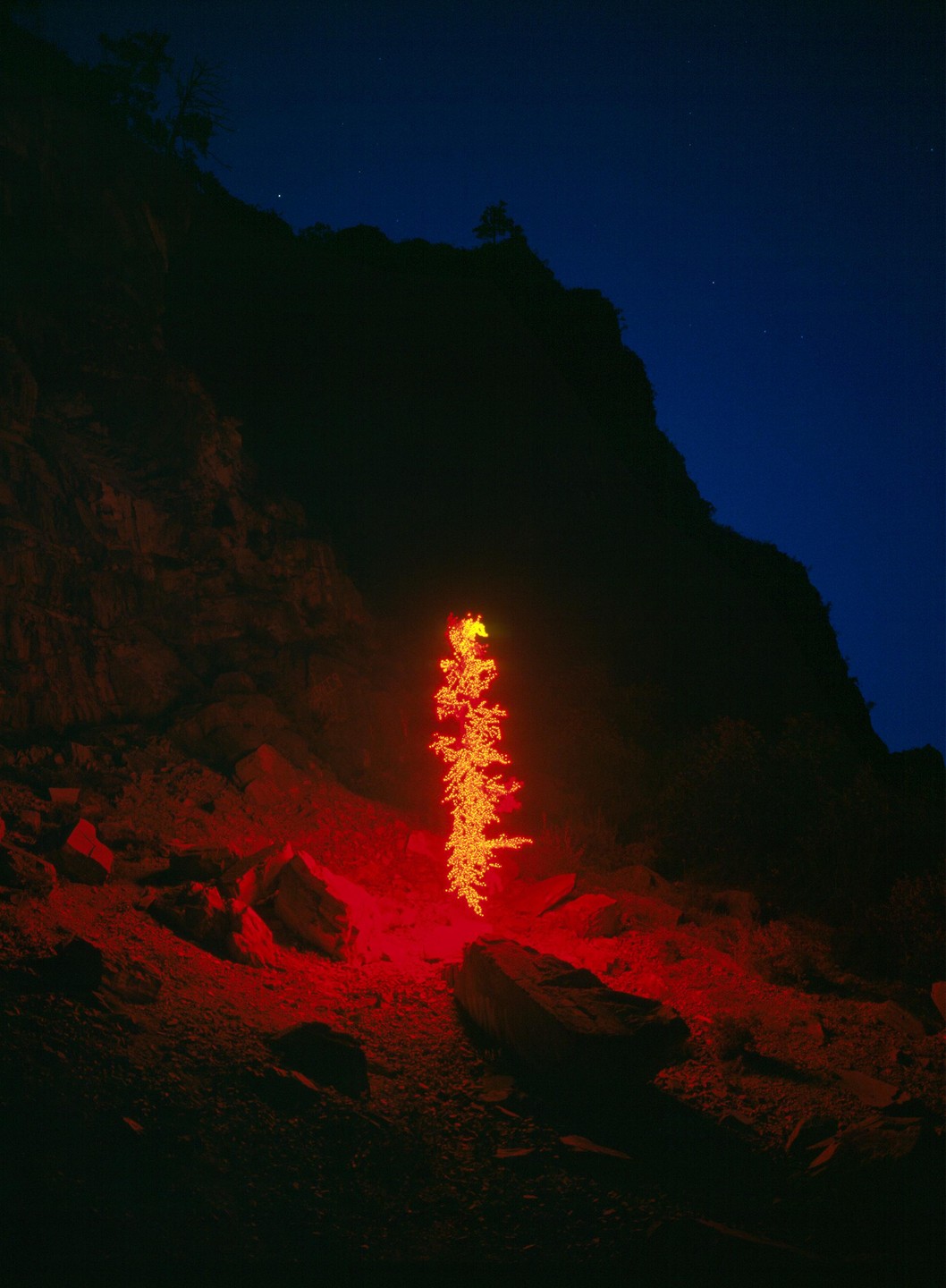 A glowing red and orange light installation illuminates a rocky cliffside at night.