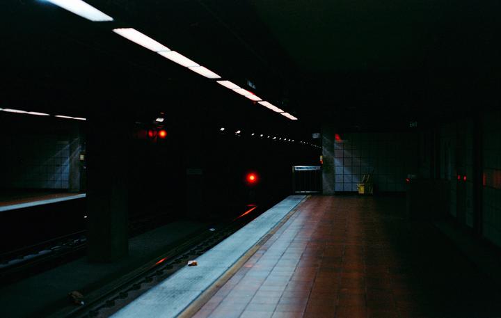 A dark subway platform is illuminated by overhead lights and red signals in the distance.