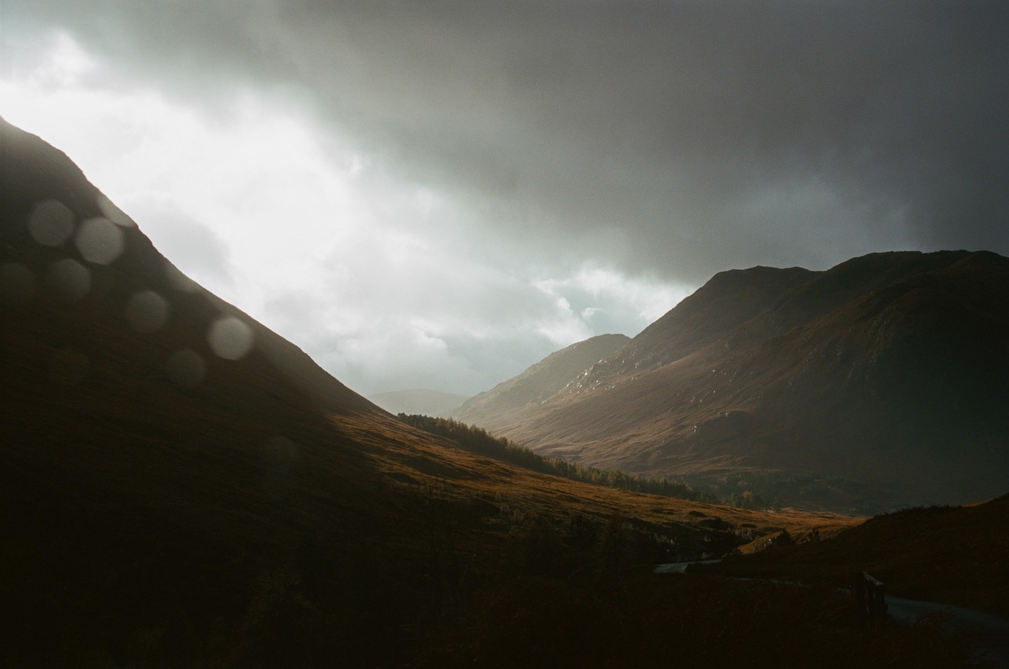 Sunlight breaks through dark clouds to illuminate a valley between two mountains.