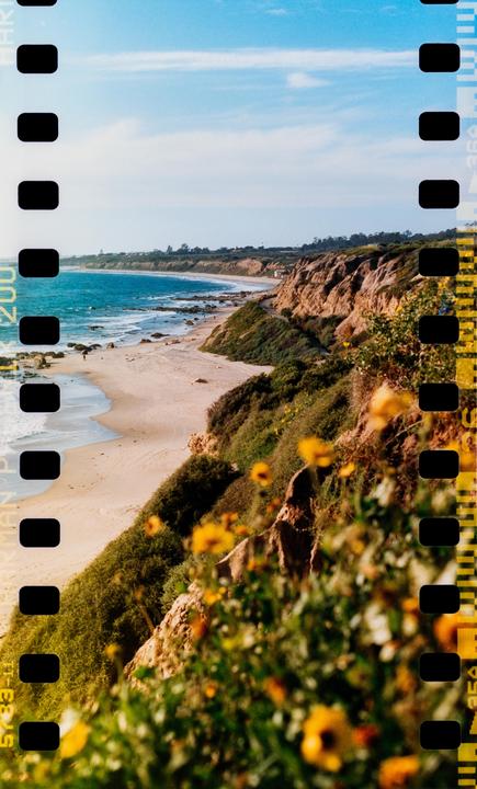 A sandy beach curves along a coastline with cliffs and green vegetation under a blue sky.