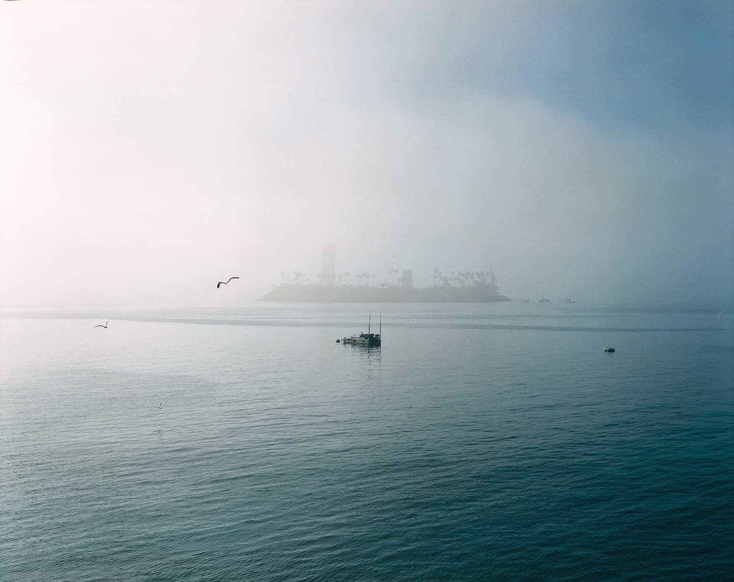 A boat floats on the water with an island and a tall building in the hazy distance.