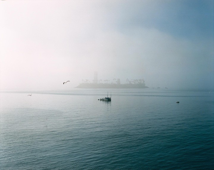 A boat floats on the water with an island and a tall building in the hazy distance.