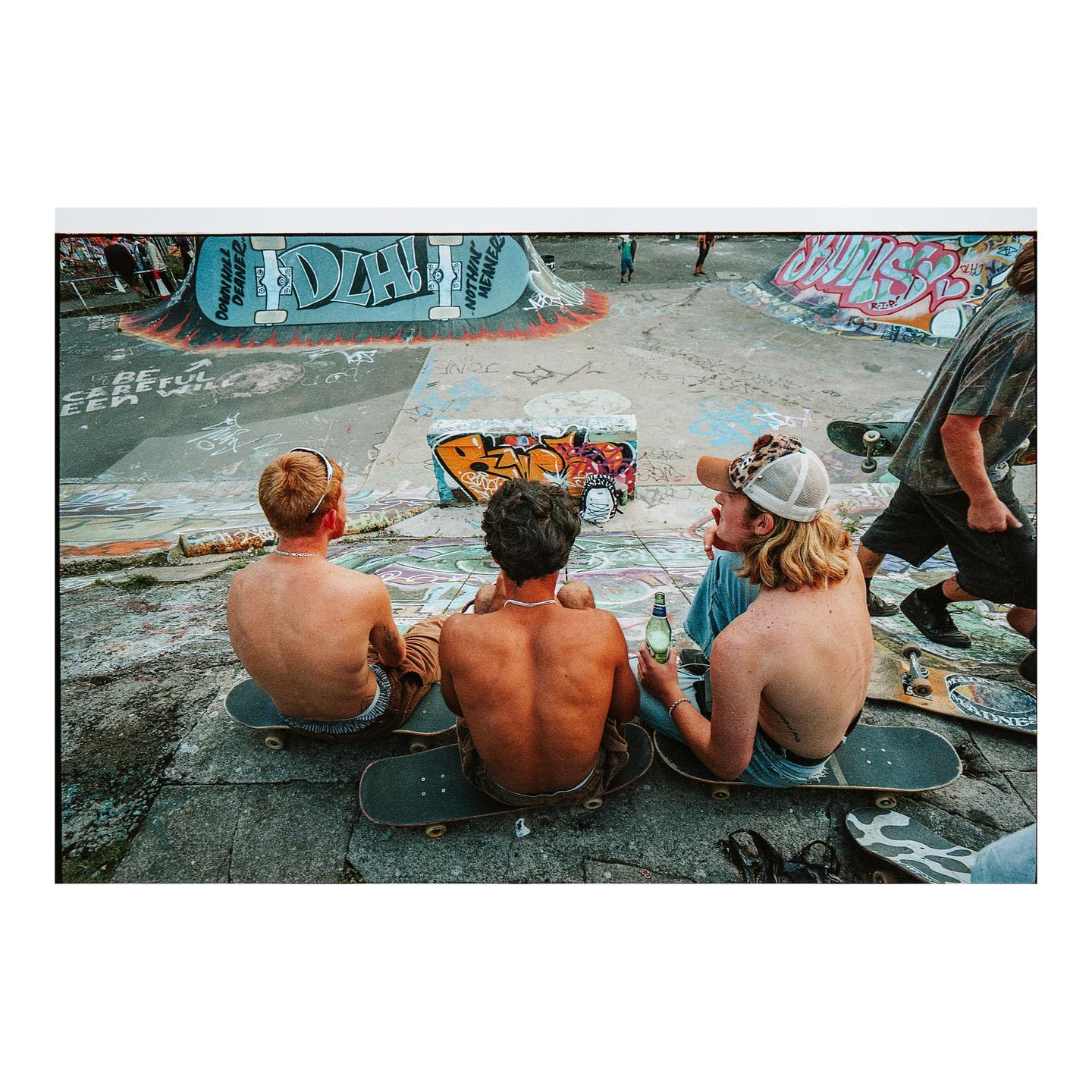 Three men sit on skateboards in a skatepark covered in graffiti.