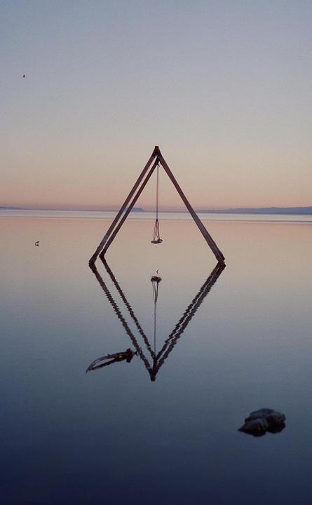 A swing set stands in the still water of the Salton Sea at dusk, with its reflection visible below.