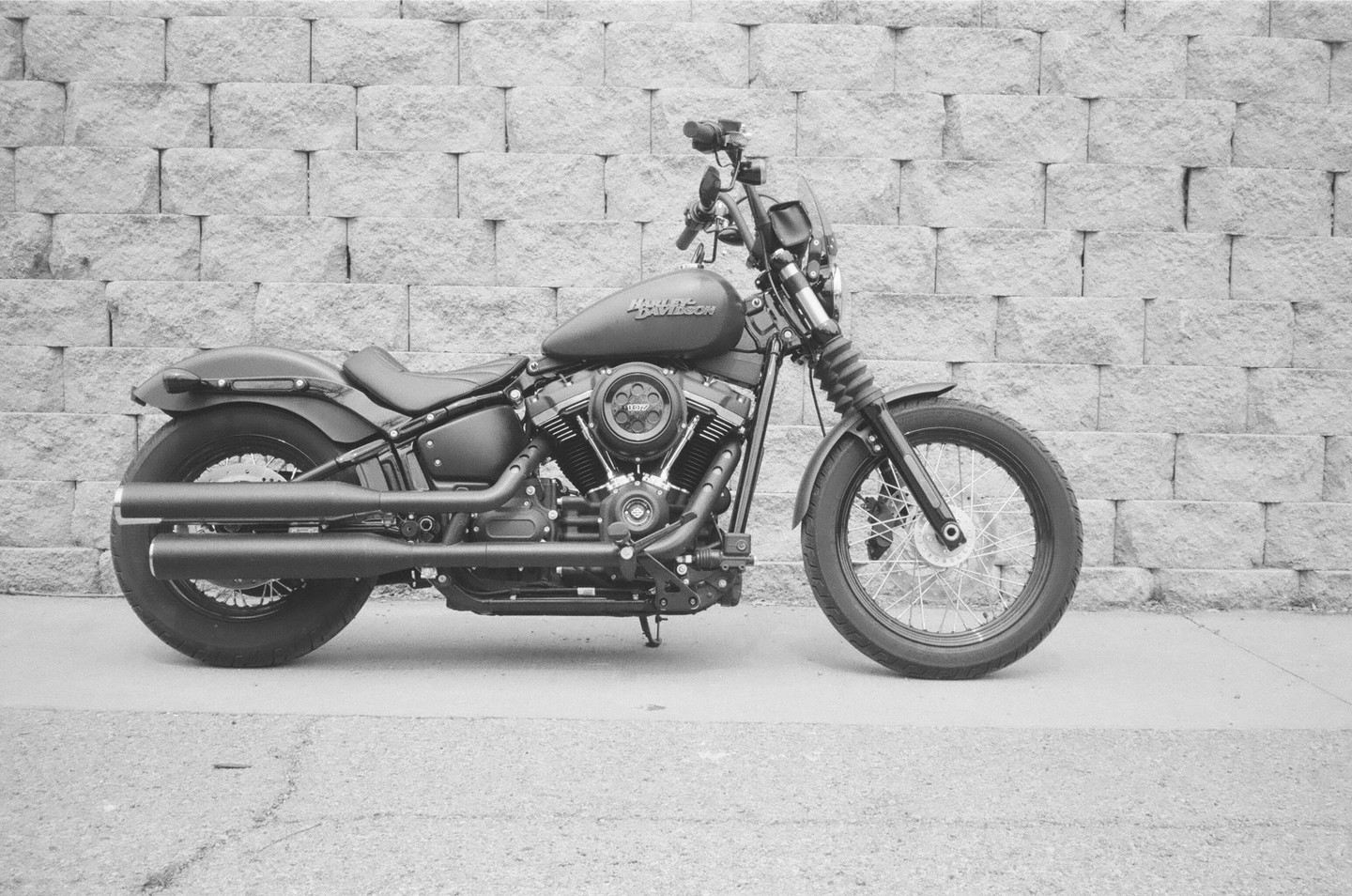 A black motorcycle is parked on a paved surface in front of a stone wall.