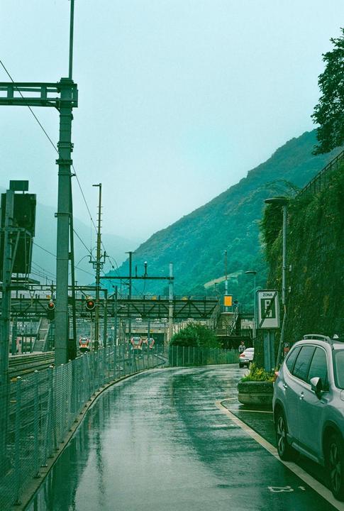 A wet road curves past a train station with a mountain in the background.