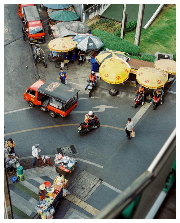 An overhead view shows a busy street scene with vehicles, pedestrians, and market stalls under umbrellas.