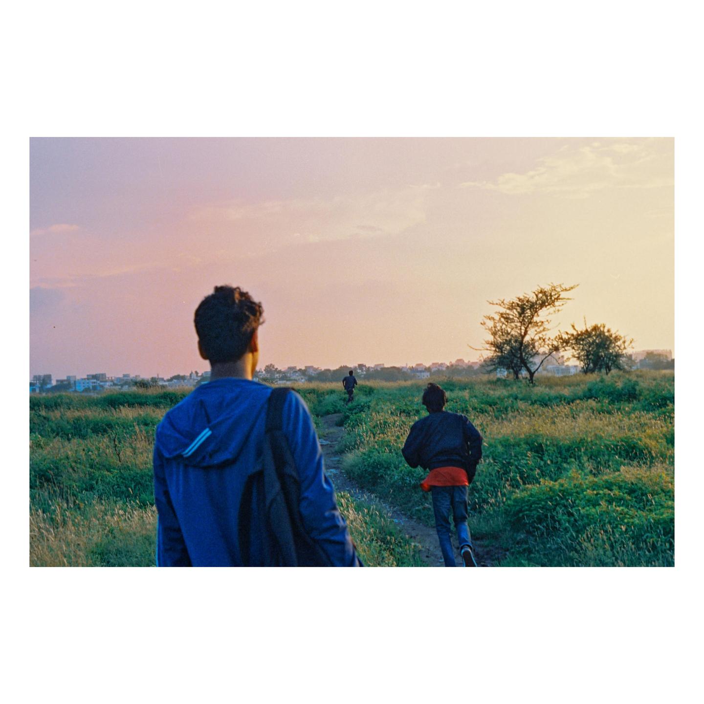 Three boys walk along a path through a field at dusk.
