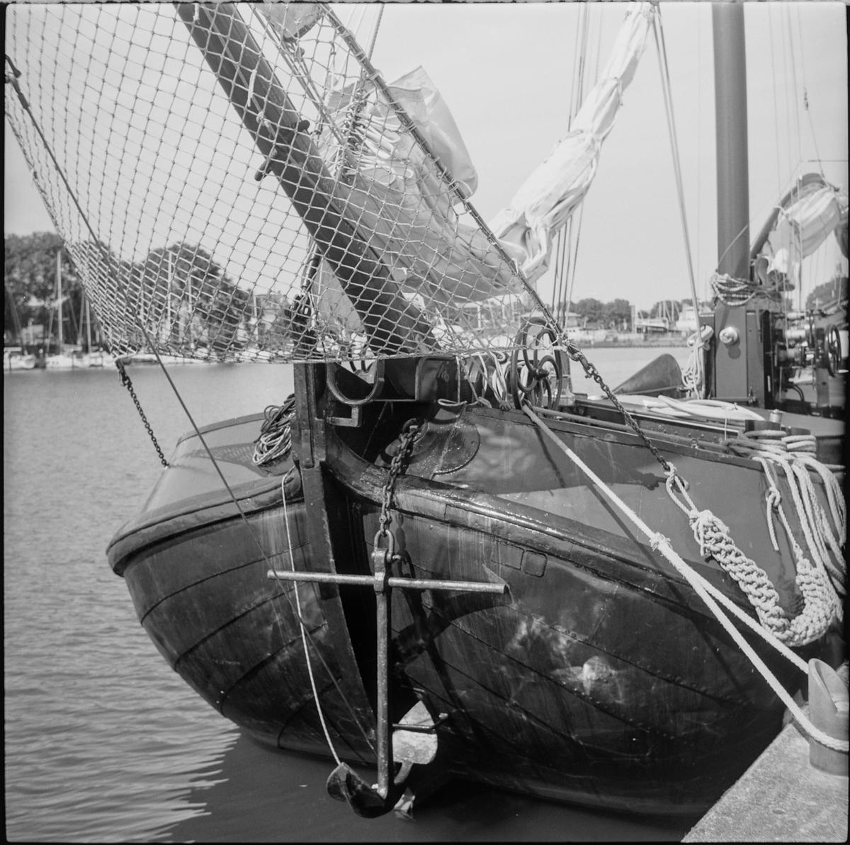 The bow of a sailboat with an anchor hanging from it is docked in the water.