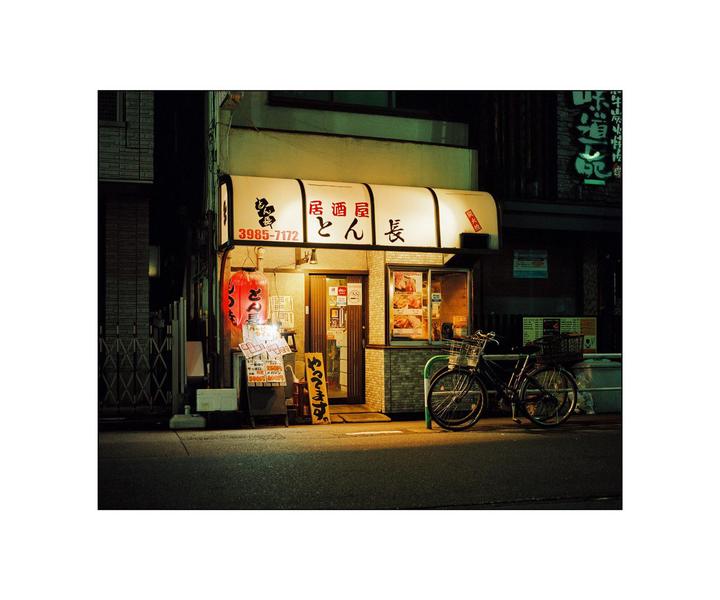 A bicycle is parked in front of a brightly lit Japanese restaurant at night.