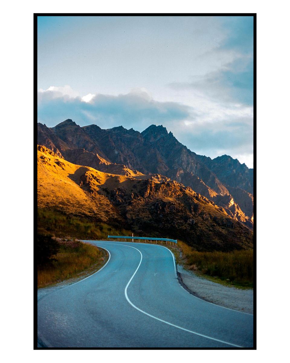 A winding road leads through a mountainous landscape with golden light on the peaks.