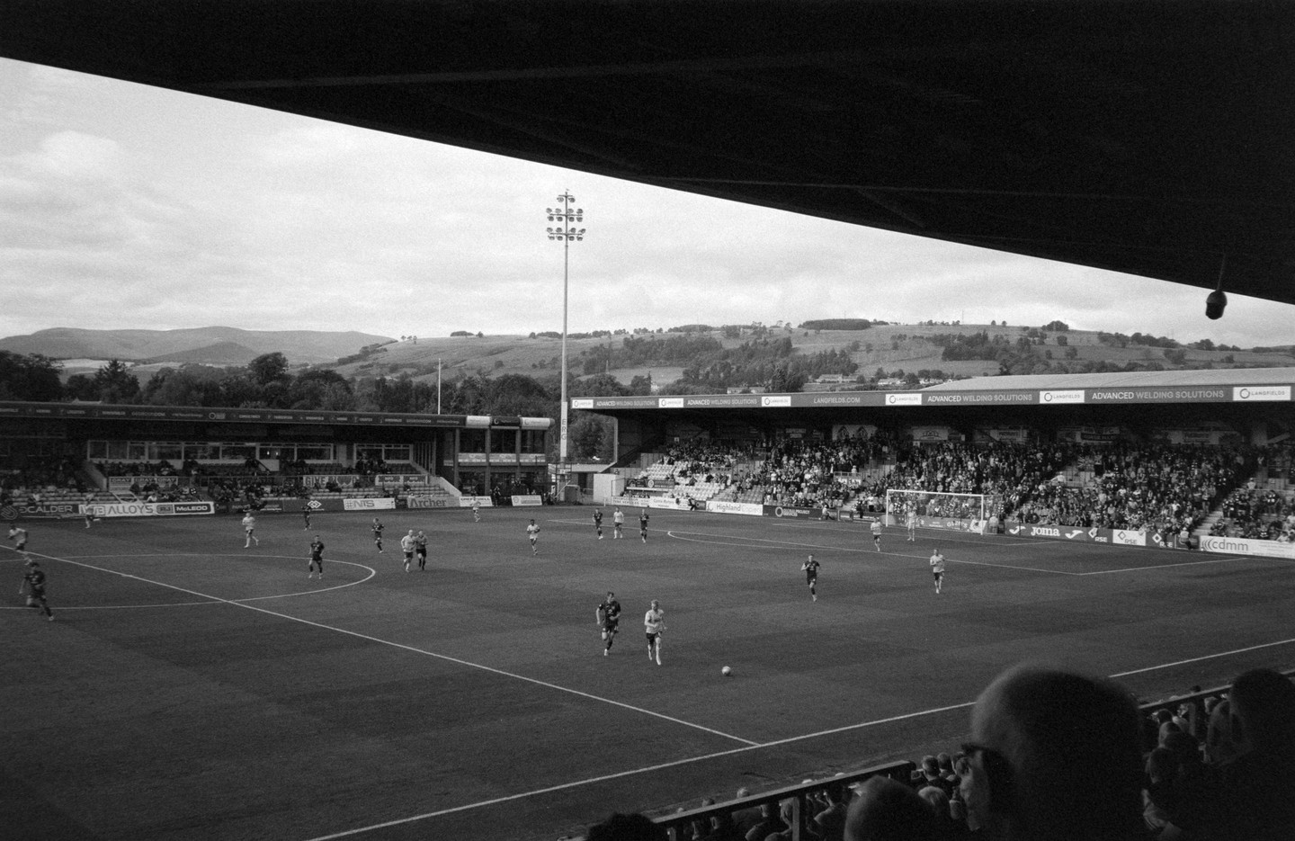 A football match is underway in a stadium with a large crowd and hills in the background.