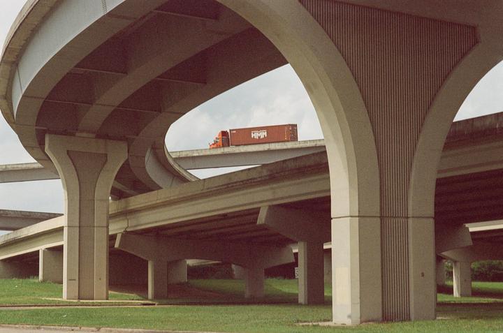 An orange truck with a container drives on an elevated highway overpass.