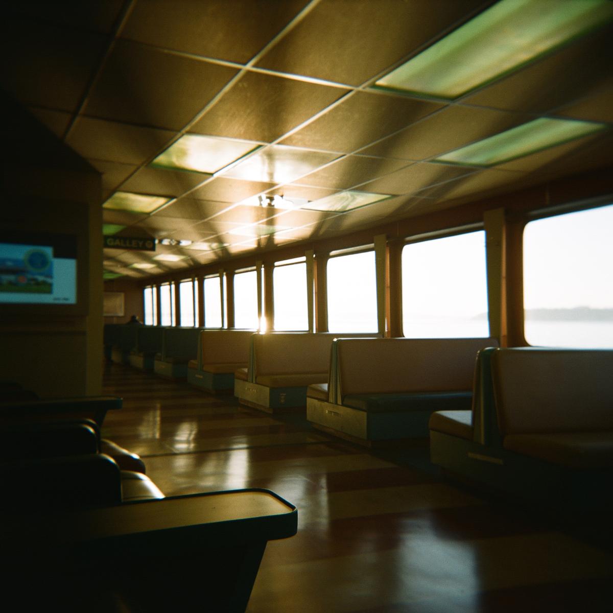 The interior of a ferry is illuminated by bright evening light streaming through the windows.