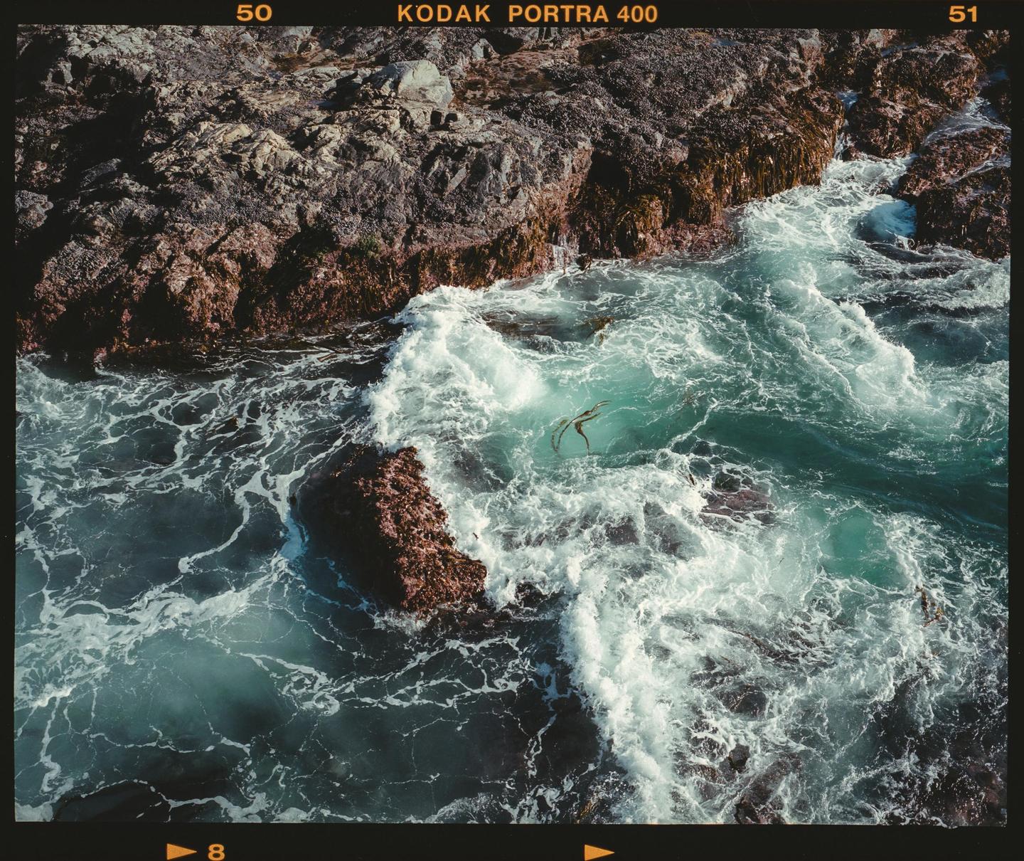 Waves crash against a rocky shore with seaweed visible in the water.