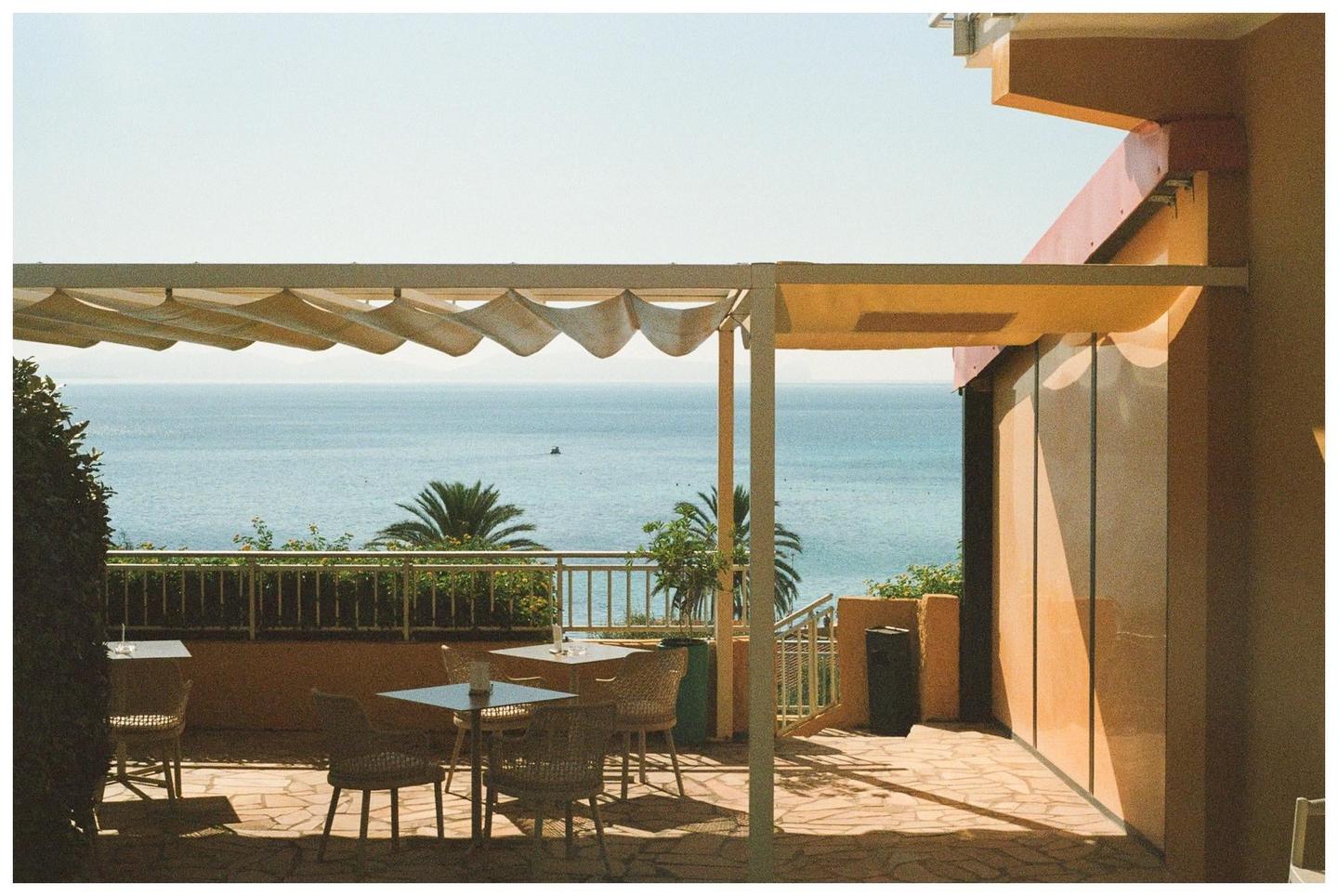 A patio with tables and chairs overlooks the ocean under a clear sky.