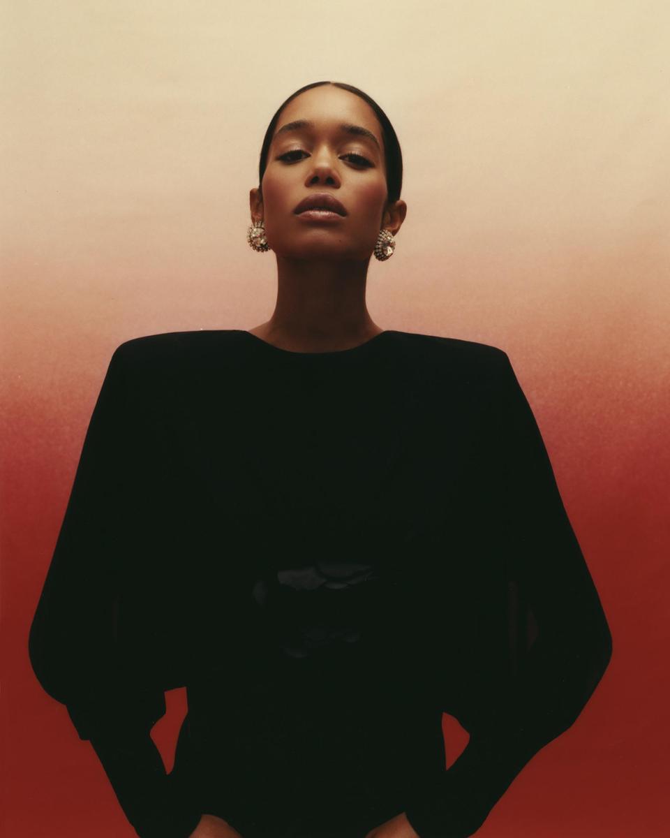 A woman with slicked-back hair and large earrings looks directly at the viewer.