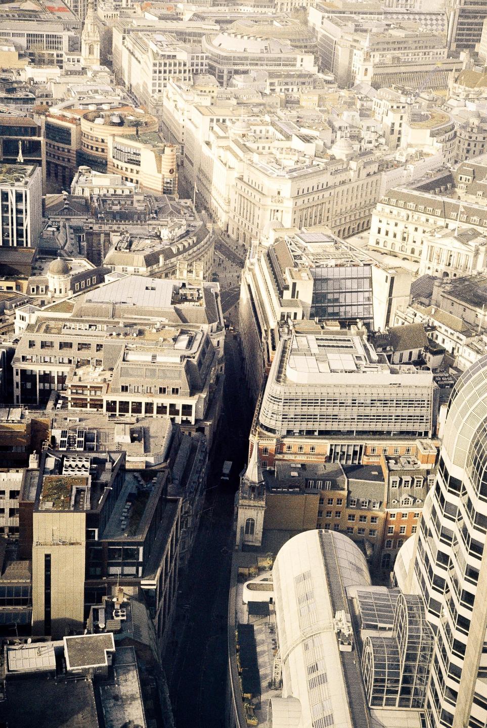 An aerial view shows a dense urban landscape with many buildings and a narrow street.