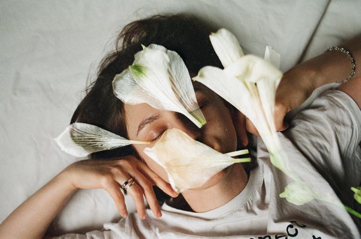 A woman lies with her eyes closed, covered in white flower petals.