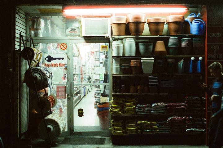A woman stands outside a brightly lit hardware store at night in New York City.