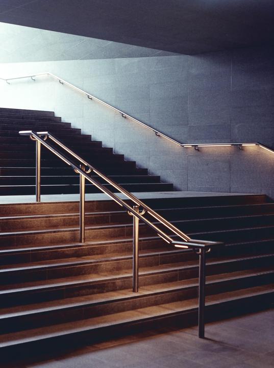 A modern staircase with metal handrails and integrated lighting ascends towards a bright area.