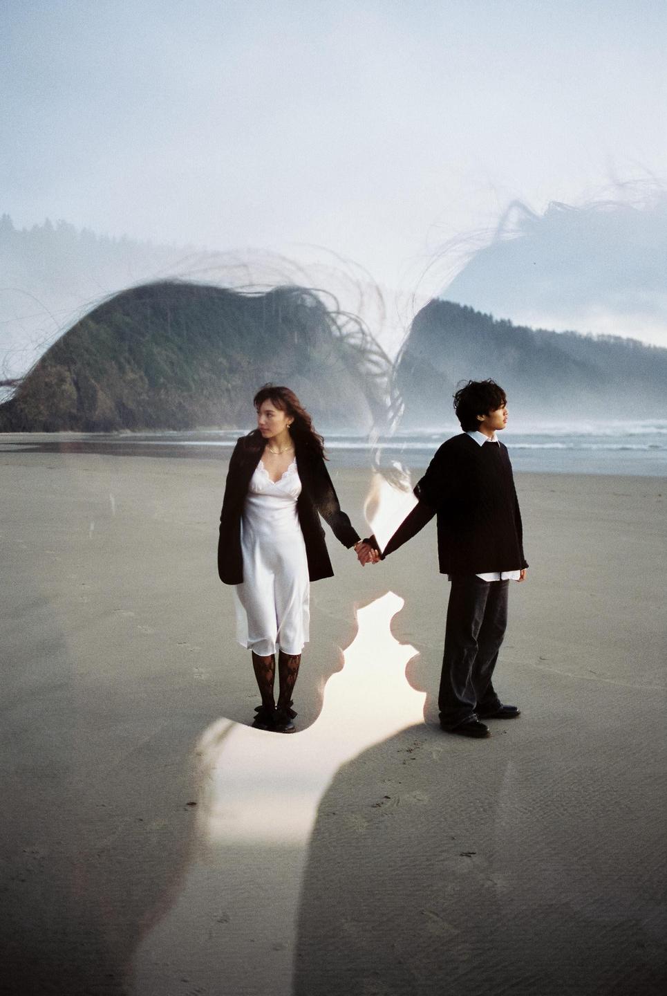 A couple holds hands on a beach with hills in the background and a double exposure effect creating abstract shapes around them.