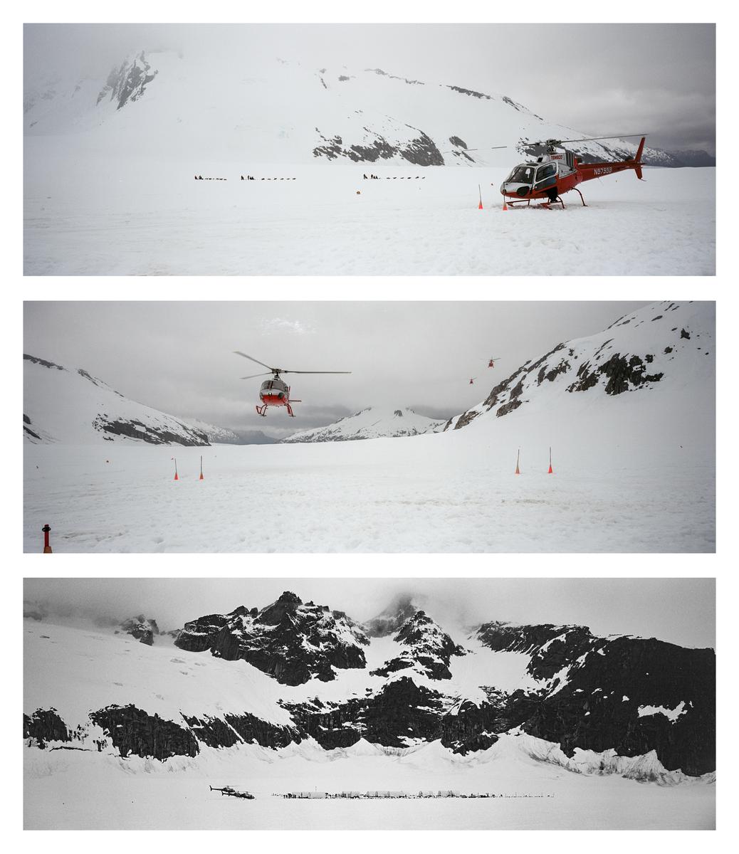 A red helicopter is parked on a snow-covered mountain with other helicopters flying in the distance.