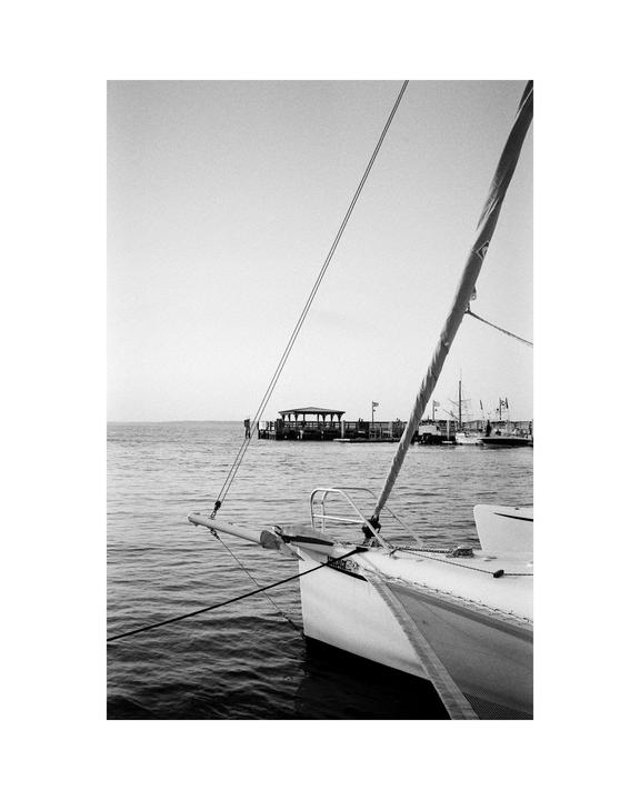 A sailboat is docked in the water with a pier and other boats in the distance.
