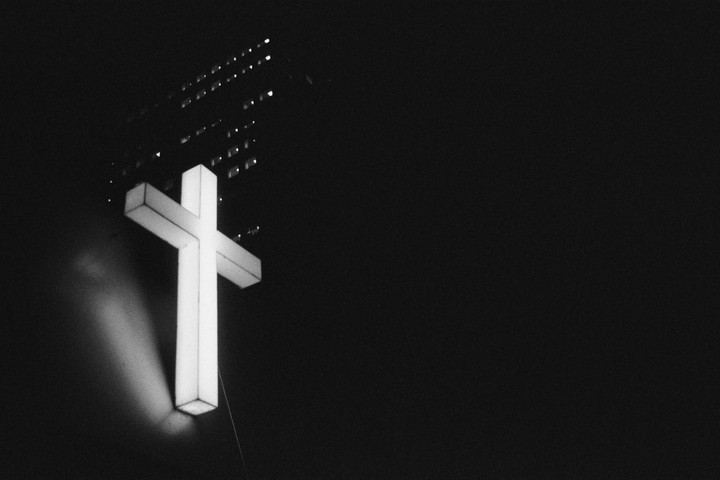 A large illuminated cross is visible against a dark background with a building in the distance.