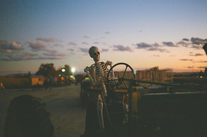 A skeleton decoration sits in the driver's seat of a vehicle at dusk.
