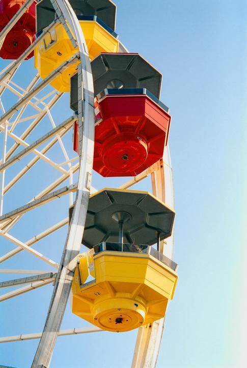 A red and a yellow gondola of a ferris wheel are visible against a clear blue sky.