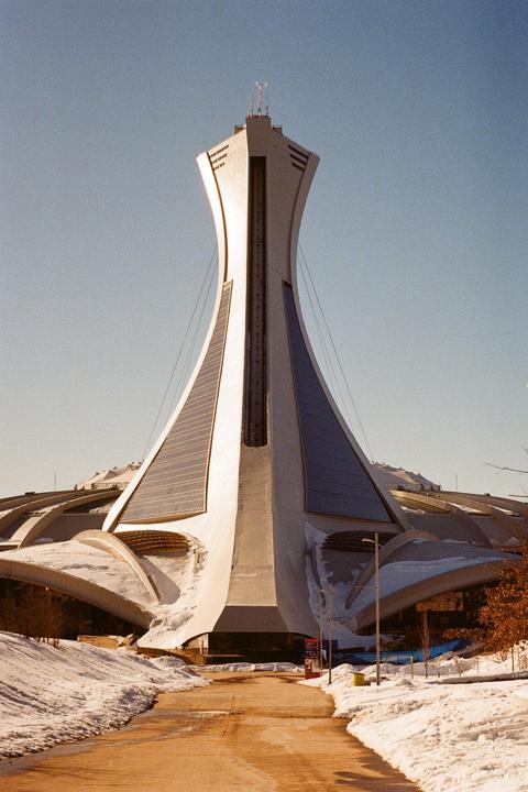 A tall, curved tower with a pointed top stands over a snow-covered landscape with a path leading towards it.