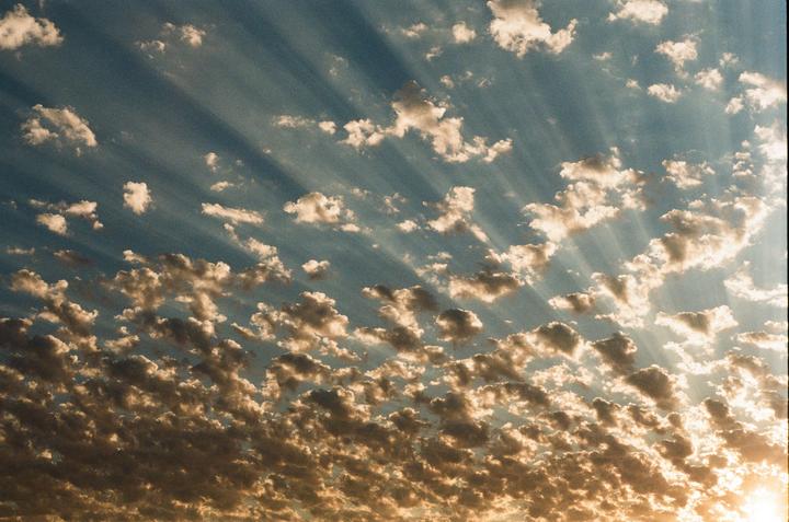 Sunlight streams through a partly cloudy sky, illuminating the clouds from below.