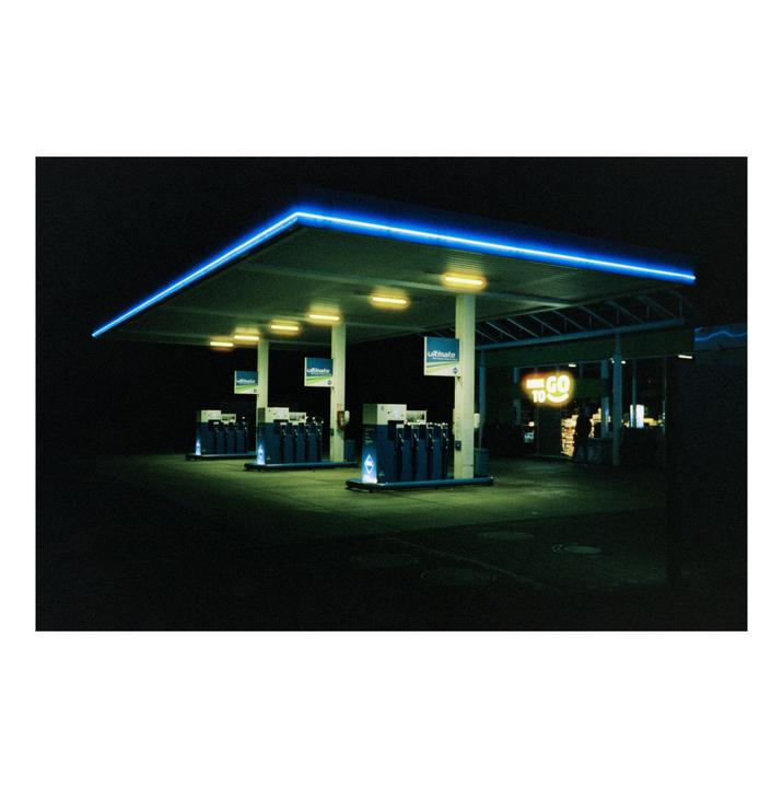 A gas station with blue neon lights and yellow interior lights stands empty at night.