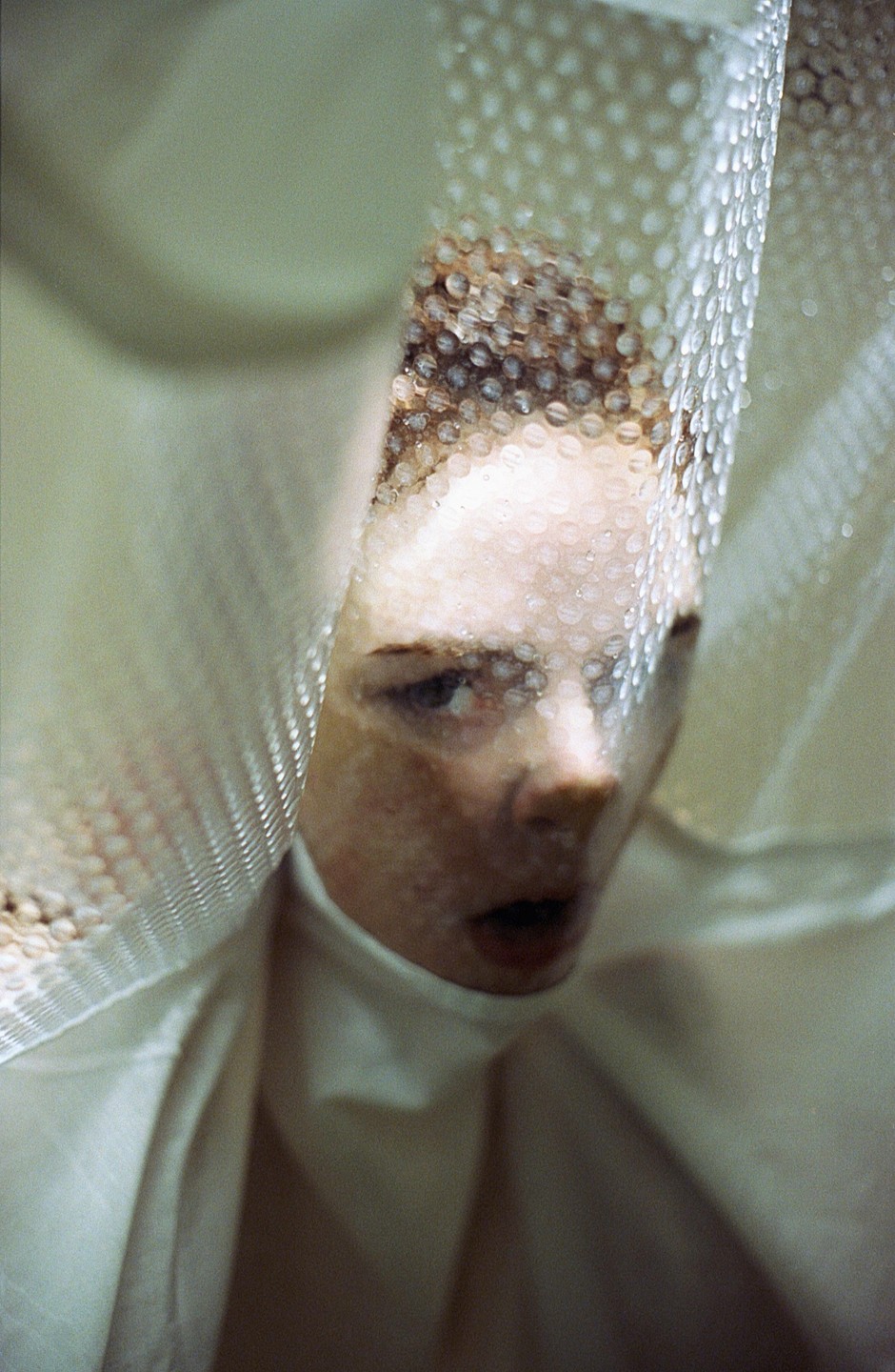 A woman's face is partially obscured by a translucent, textured material, with her mouth slightly open.