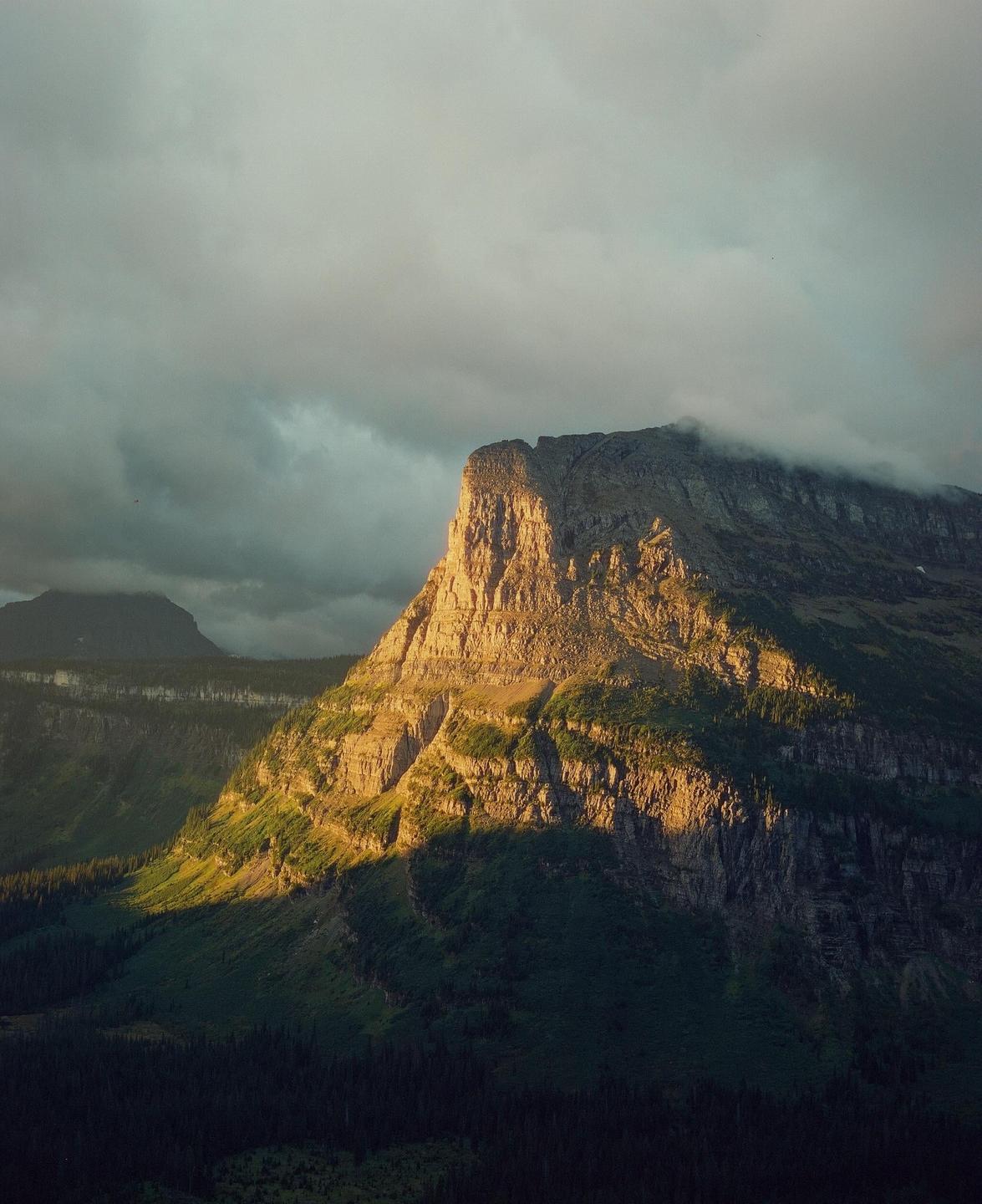 A mountain peak is illuminated by golden light under a cloudy sky.
