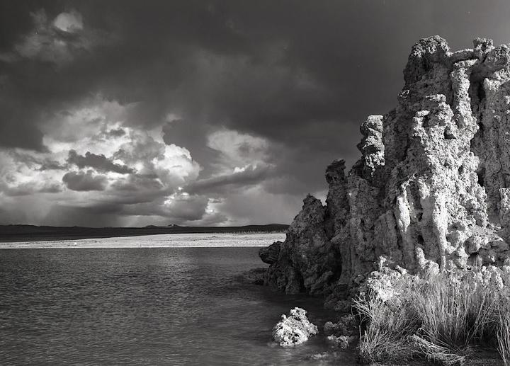 A body of water with tufa formations on the right and a cloudy sky above.
